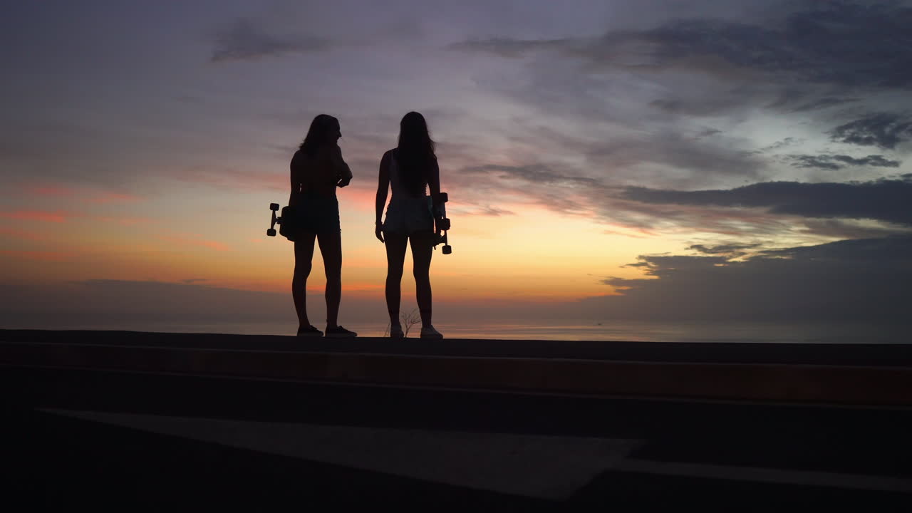 At the mountain's pinnacle, girlfriends enjoy the sunset view post skateboarding adventure