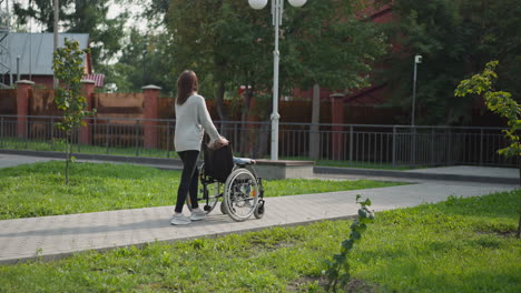 mom pushes child with injury in wheelchair walking in park