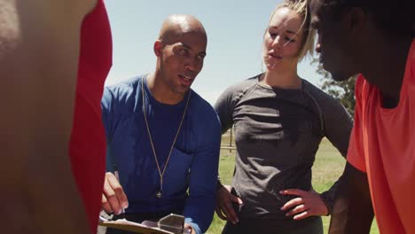 diverse fit group and male trainer in discussion at obstacle course in the sun