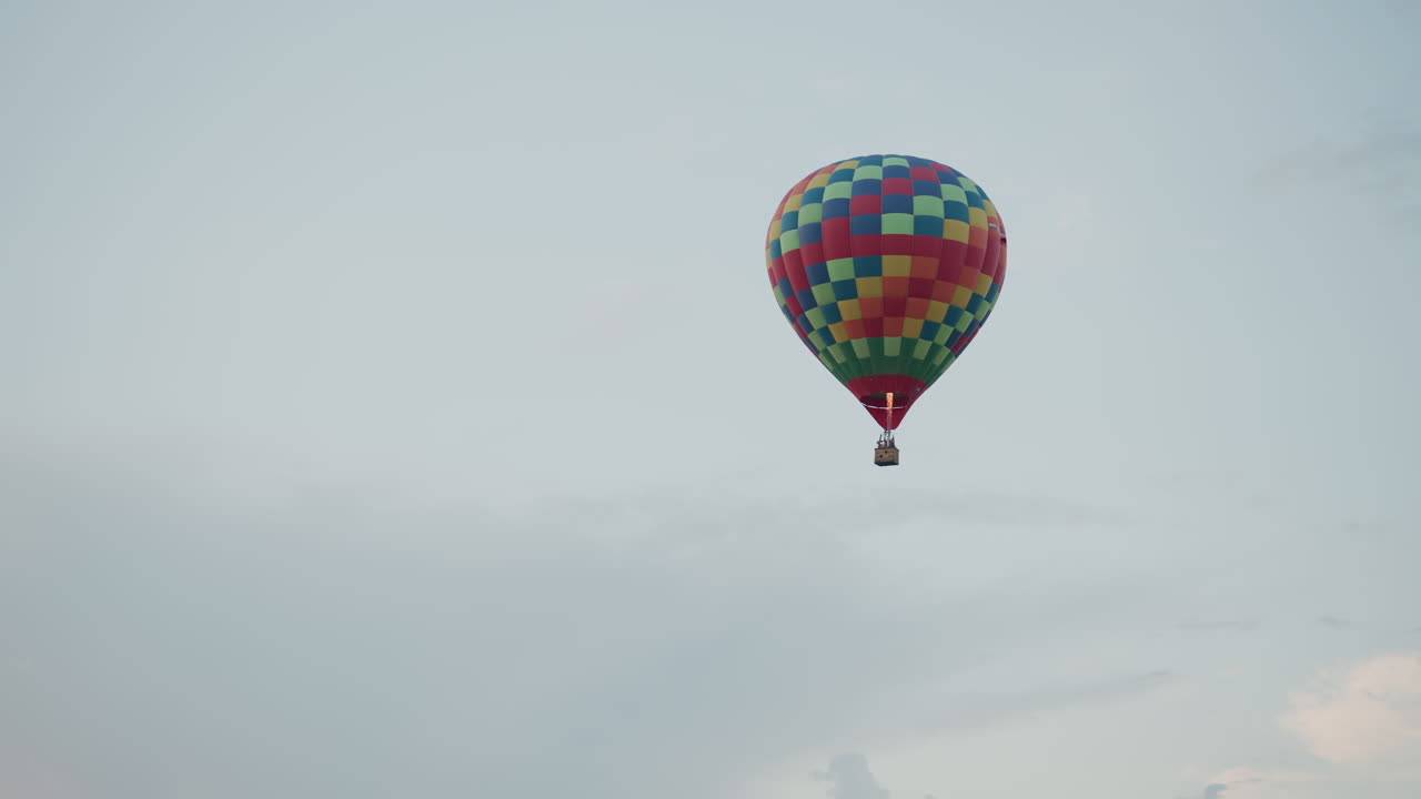 Vibrant checkered hot air balloon soaring through pale sky with ...