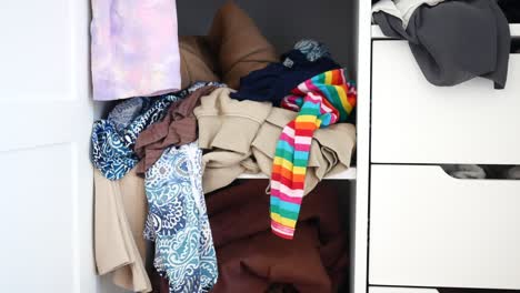 un armario desordenado con ropa plegada cuidadosamente en los estantes y en los cajones