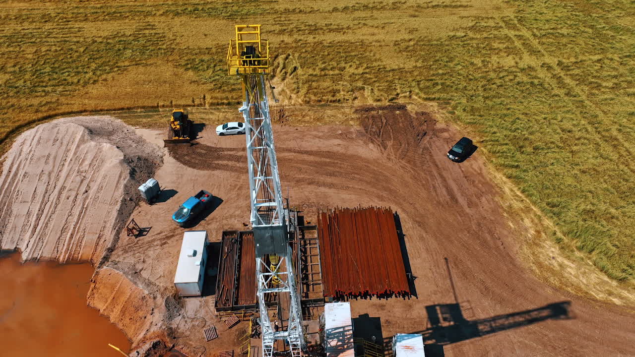 Footage around the top of the oil rig tower. Cars, metal pipes and people working on the location. Aerial view.