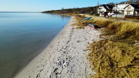 Tranquilamente-Ondeando-El-Agua-Del-Lago-Azul-Claro-En-Una-Pequeña-Playa-De-Arena-Con-Enormes-Villas-De-Lujo-Con-Hermosas-Vistas-En-Un-Claro-Día-De-Verano-En-Polonia