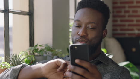 portrait young african american man using smartphone drinking coffee at home browsing messages networking texting social media sharing lifestyle online enjoying relaxing in modern apartment close up