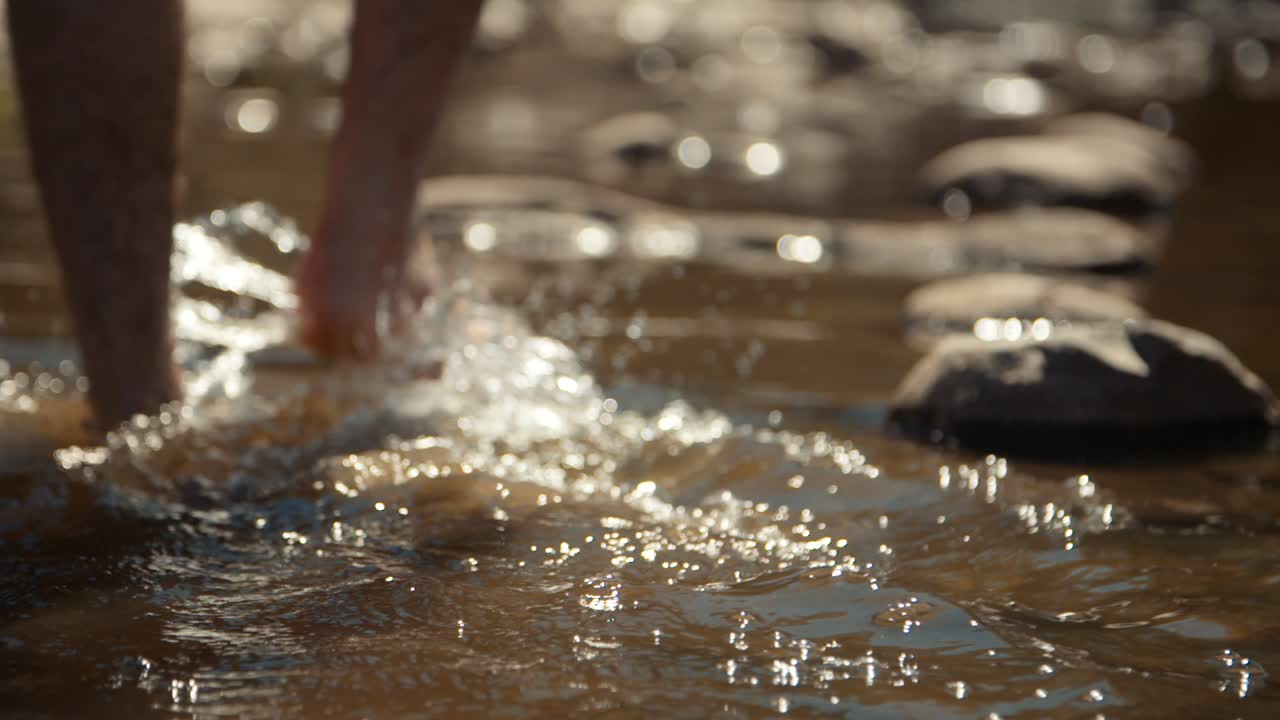 Slow motion handheld shot of a Caucasian male walking through water in a riverbed.
