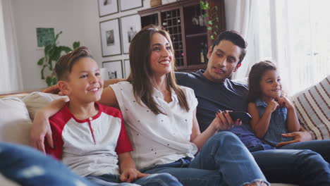 young hispanic family sitting on the sofa at home watching tv together, close up