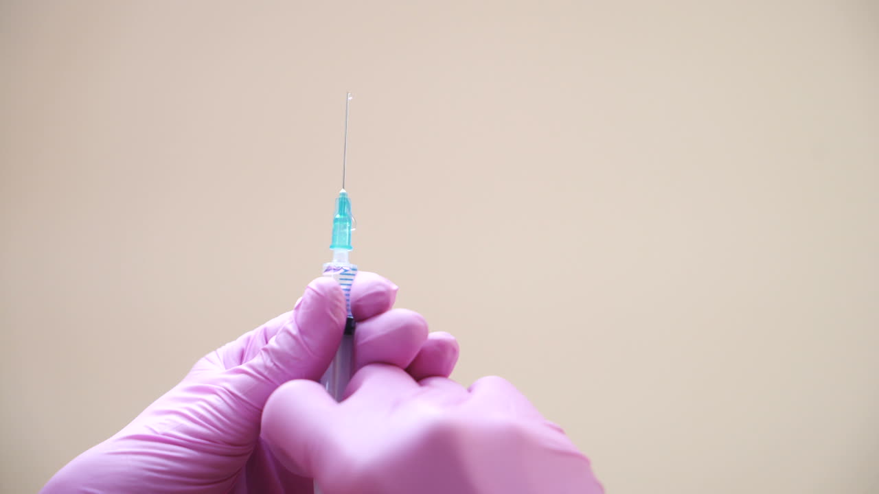 Close-up view on a cosmetologists hands in gloves holding syringe with needle for rejuvenating facial injections.