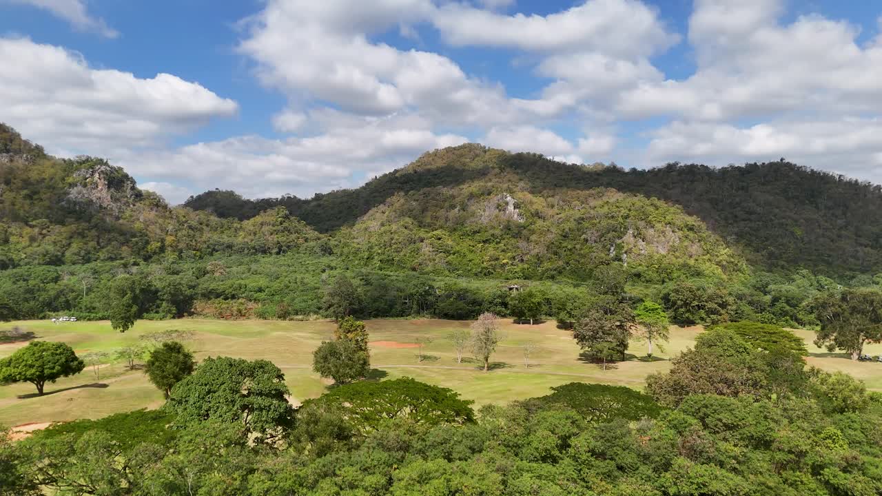 Filmagem feita com drone revela um campo de golfe tropical exuberante cercado por montanhas arborizadas sob um céu azul