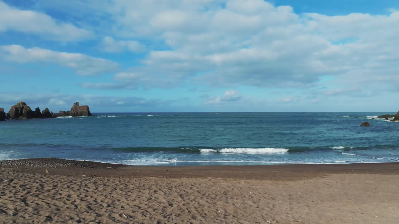 People relax on the beach watching waves crashing on golden sand beach La Morita, Tenacatita, Mexico. Dolly in flyover aerial reveals panoramic view of ocean horizon and cloudy sky