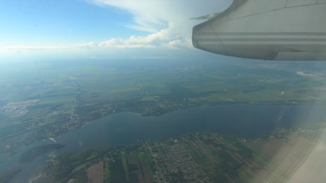 Aerial-view,-through-airplane-window-view,-aircraft-window-glass,-during-flight-inside-plane-cabin-looking-through-the-window,-blue-sky,-clouds,-lands-and-river