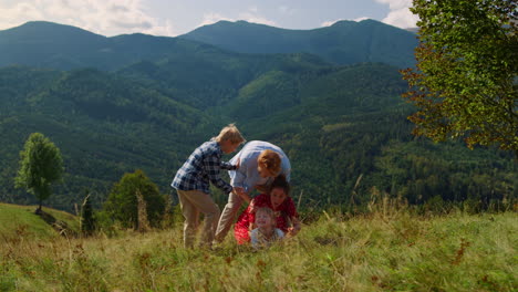 family falling grass playing on mountain hill. parents have fun with children.