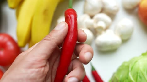 hand holding a red chili pepper amongst various fruits and vegetables