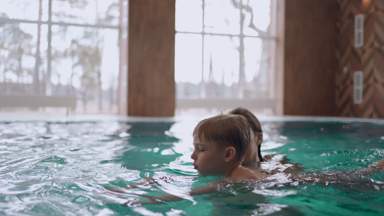 mother is teaching his little son to swim in pool indoor swimming pool in wellness center