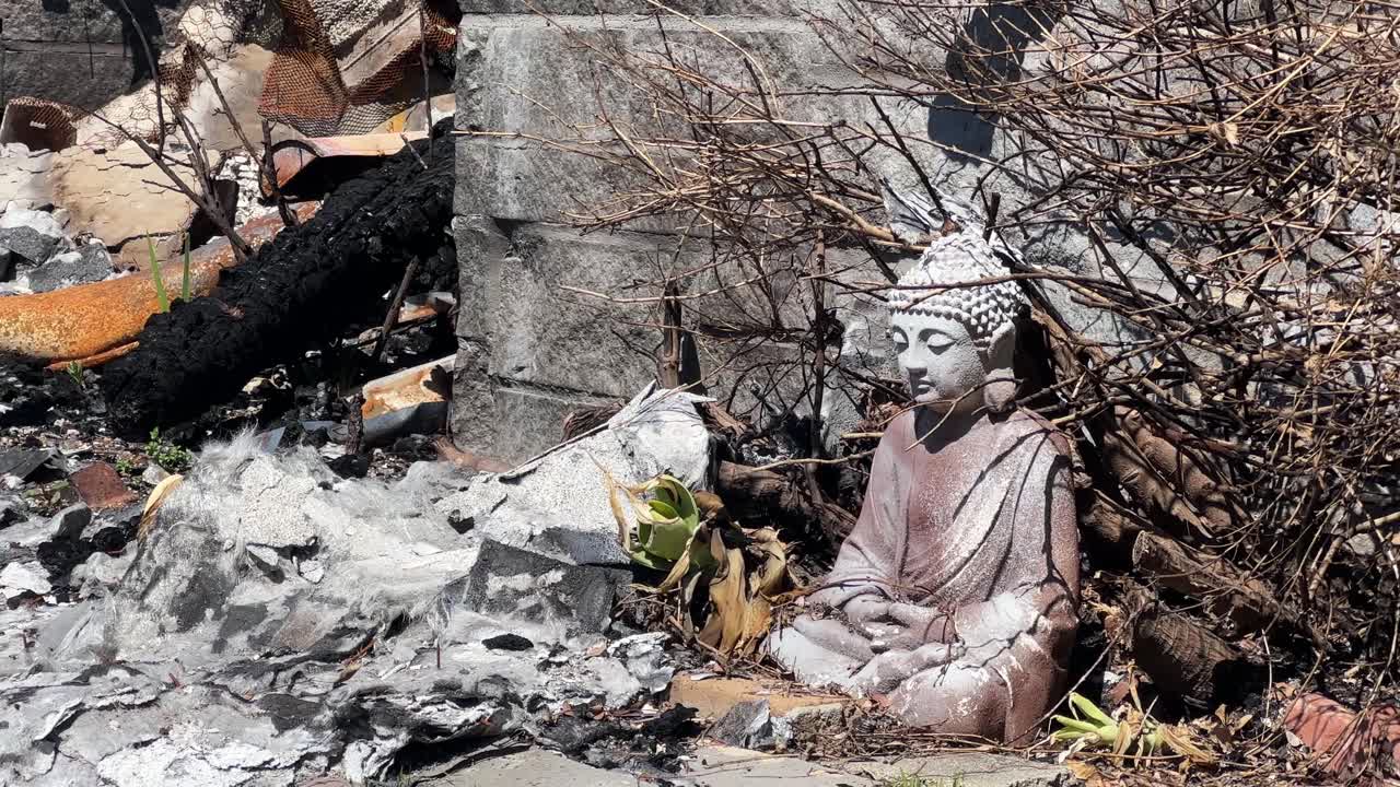 Handheld close-up panning shot of a surviving Buddha statue amongst burned rubble after the Eaton Fire in Altadena, California. 4K