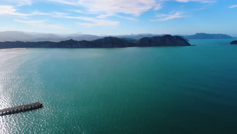 Muelle-De-La-Bahía-De-Tolaga-Y-Acantilado-Masivo-Al-Fondo-En-La-Bahía-De-Tolaga,-Nueva-Zelanda