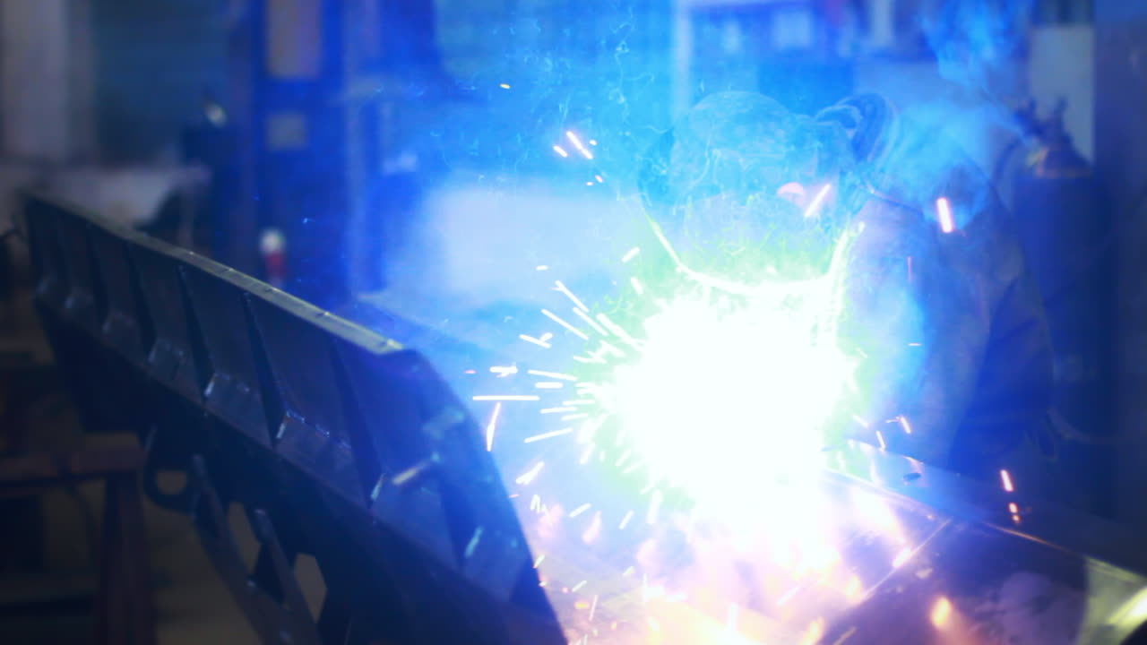 Craftsman welds steel structure at workshop. Metal sparks throwing