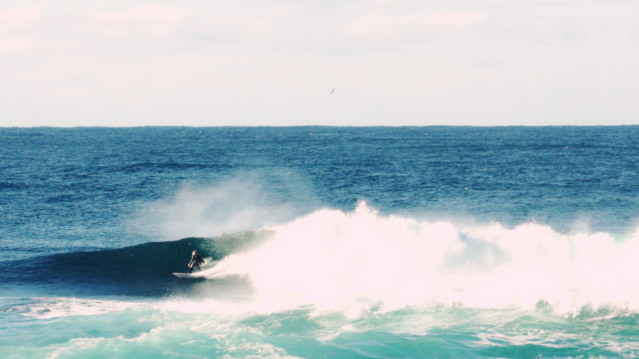 Golden light cuts through cresting surf as athlete races down powerful wave face at dusk