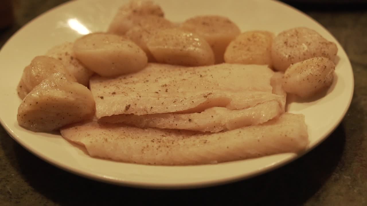 Slow Motion Panning shot of Rock fish and Sea scallops being seasoned and prepared for cooking. HD 1080p 23.98p