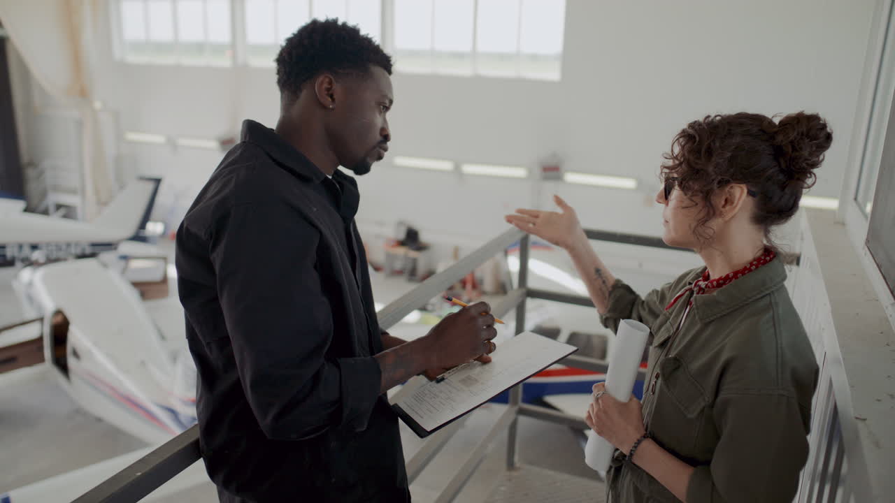 Two Avionics Technicians Discussing Planes in Aircraft Hangar