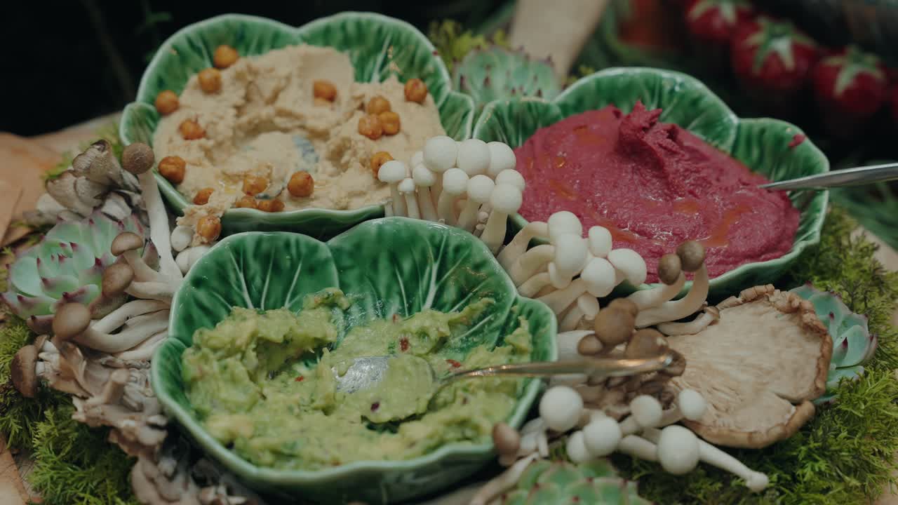 vibrant dips and mushrooms arranged in decorative green ceramic leaf bowls