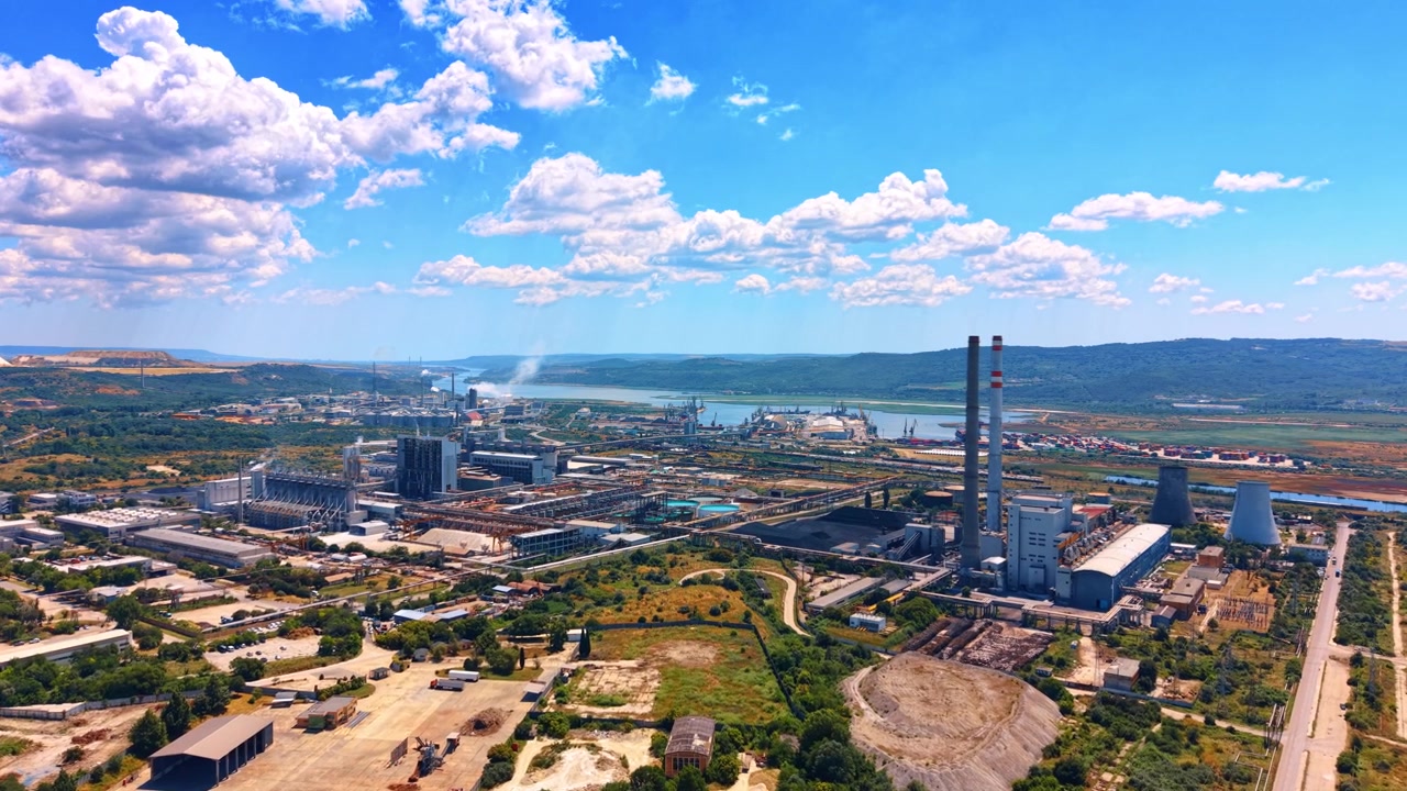 Vista aerea panoramica di centrale elettrica e zona industriale. Alte ciminiere e strutture di fabbrica si ergono in un'ampia valle industriale vicino all'acqua sotto un cielo luminoso