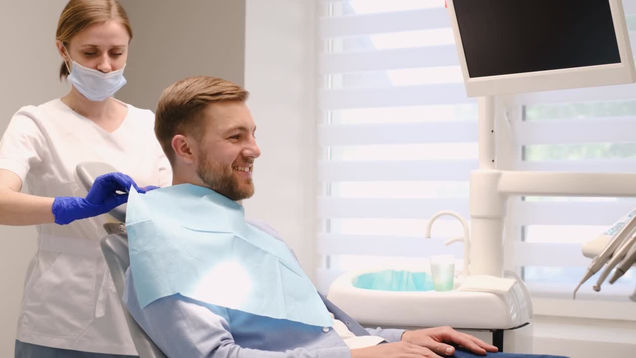 Young European man in a dental chair, he smiles at the doctor. Brushing teeth from caries