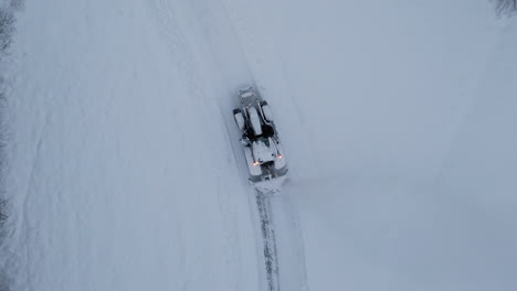 Aerial-birdseye-tracking-shot-of-tractor-plowing-road-in-winter