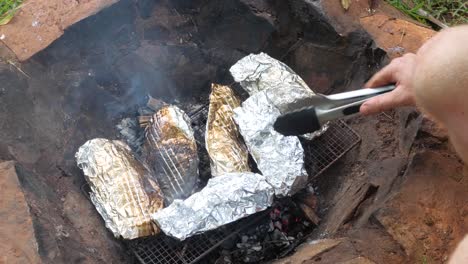 cooking tilapia fish wrapped in foil over hot coals on a fire