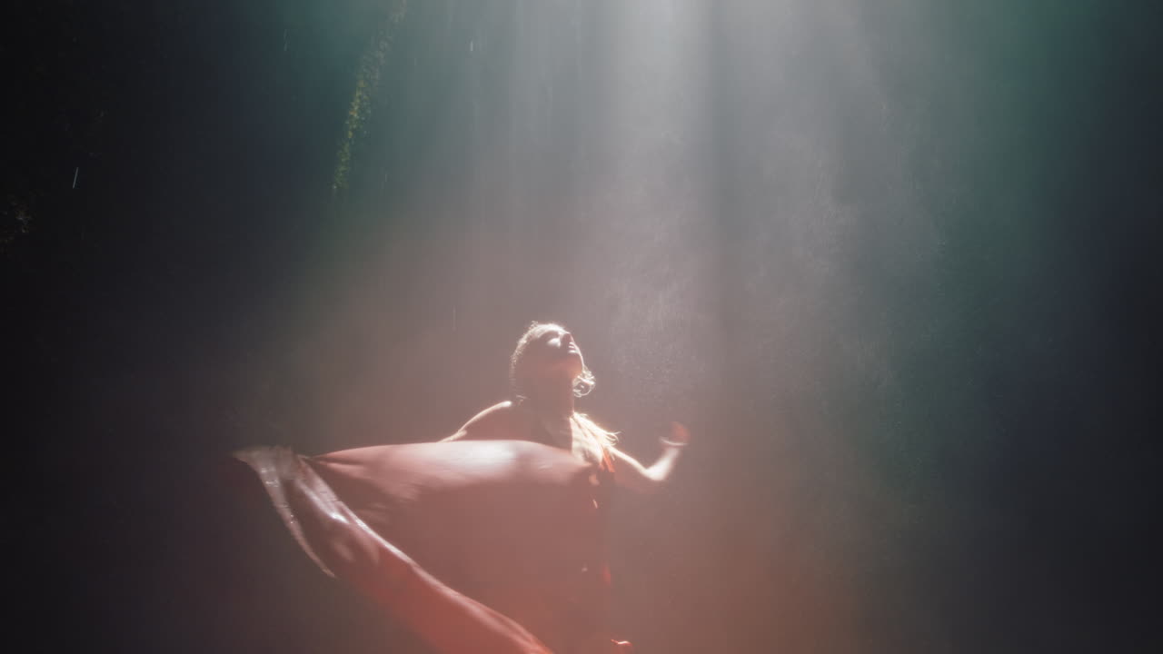 hermosa mujer bailando en la cueva de la cascada con un hermoso vestido disfrutando de la danza sintiendo libertad espiritual 4k