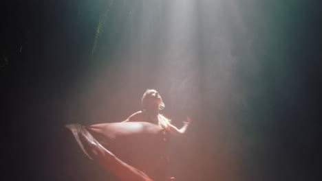 hermosa mujer bailando en la cueva de la cascada con un hermoso vestido disfrutando de la danza sintiendo libertad espiritual 4k