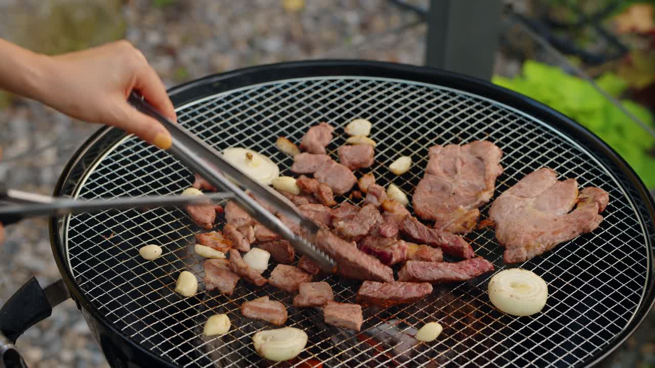 Close-up of a person using kitchen shears to cut pieces of tender, grilled beef into bite-sized portions directly on a hot charcoal barbecue grill, a common Korean technique