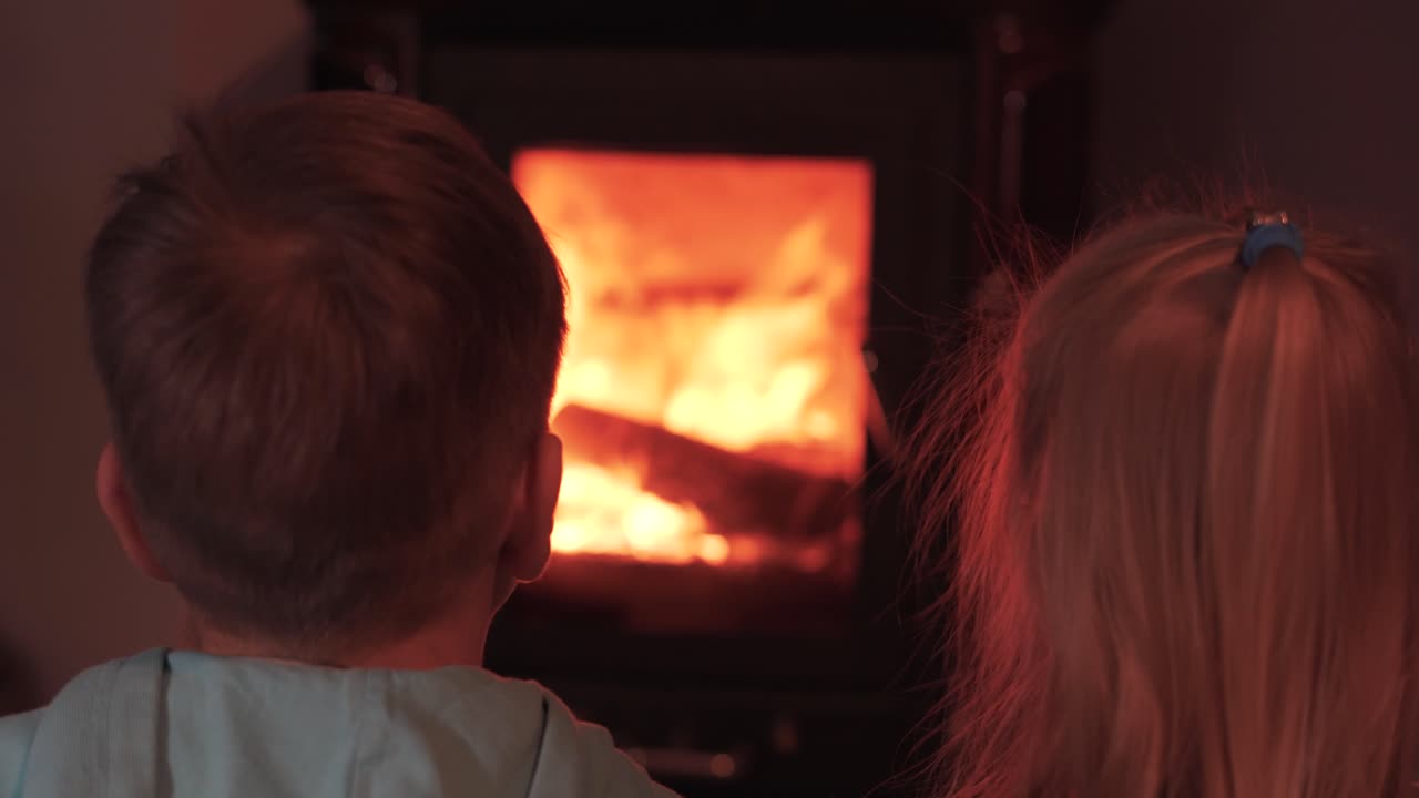 Two Happy Little Children Brother and Sister Sitting by the Fireplace and Watching the Fire. Enjoying a Warm Atmosphere and Flame Move. Concept of Happy Family. Static Shot. Rack Focus