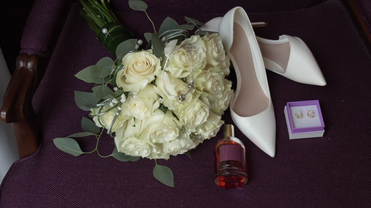 Elegant wedding bouquet with white roses beside bridal shoes jewelry and perfume bottle