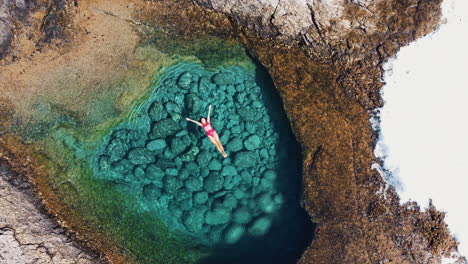 woman in turquoise waters in a cove when a wave suddenly crashes in, fuste