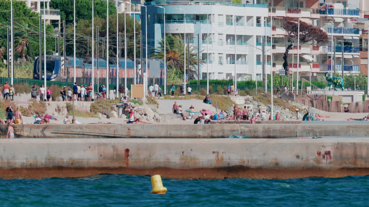 Cannes, France - October 7, 2025: A train passes by a crowded beach as people relax by the sea