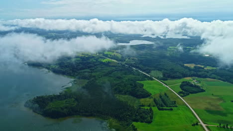 lush green landscape with lake, roads, and low clouds, daylight, aerial view