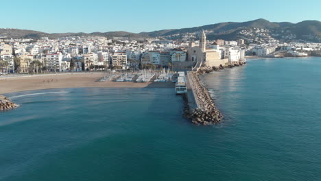 Ancient-coastal-city,-with-a-church-perched-at-edge-of-shore,-surrounded-by-stunning-sea-and-majestic-mountain-range