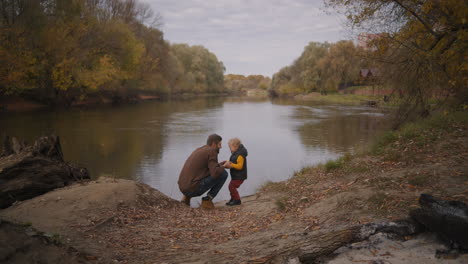 Un-Niño-Alegre-Y-Su-Padre-Están-Charlando-En-La-Naturaleza-Parados-En-La-Orilla-Del-Lago-Viajando-A-Una-Reserva-Natural-Feliz-Paternidad-E-Infancia