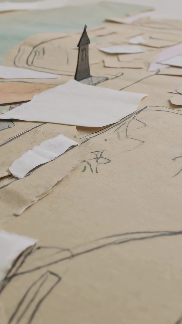Vertical video: Camera panning paper scene on table to center dark tower, revealing kraft sketches