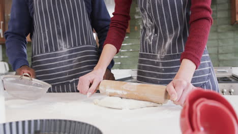 happy diverse couple standing in kitchen, sifting flour and rolling dough,slow motion