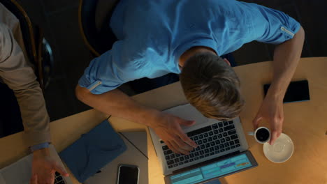 Overworked man drinking coffee while typing laptop. Creative team working inside