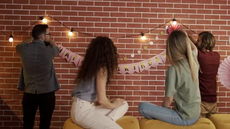 friends preparing party indoors hanging garlands and hbirthday letters, decorating