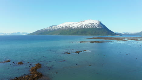 aerial, rising, drone shot of tranquil, blue sea and a snowy mountain, sunny, summer day, in the lyngen alps, troms, nordland, north norway