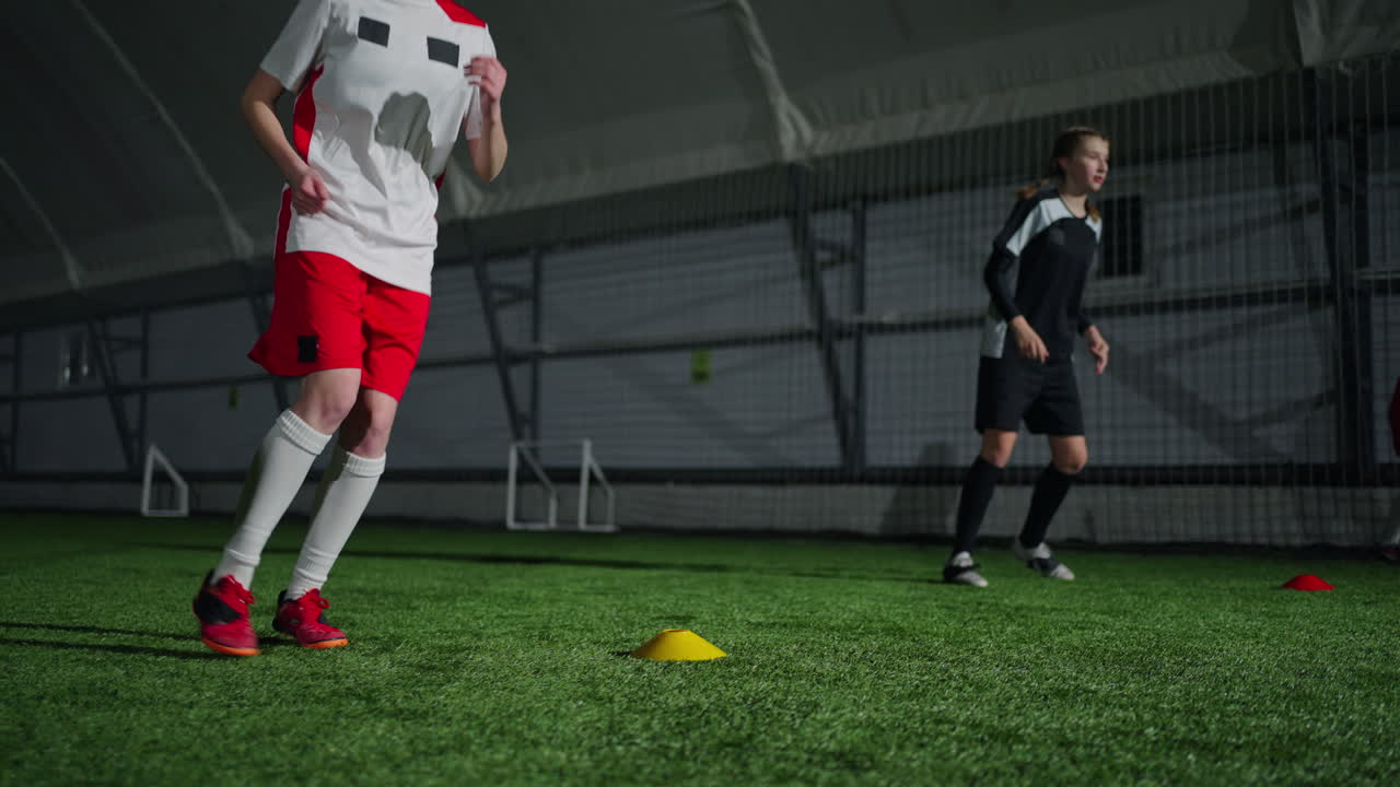 두 명의 여자 축구 선수들이 실내 경기장에서 연습을 하고 있습니다.