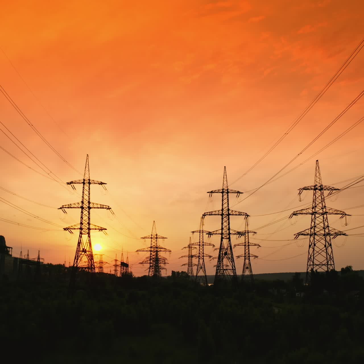 Transmission lines against red evening sky. High-voltage electricity towers at sunset. Silhouettes of electricity pylons and cables at beautiful orange sunset. Motion camera back