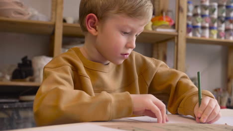 niño rubio dibujando sentado en una mesa en un taller de artesanía 1