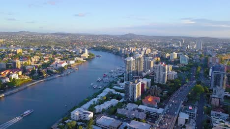 panning aerial view of a river, ferry and busy road passing through a city at sunset