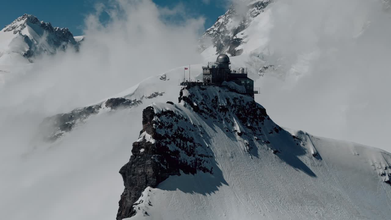 orbita aérea derecha para establecer el observatorio de la esfinge retroiluminado en jungfraujoch, suiza, nubes blancas y nieve en el fondo