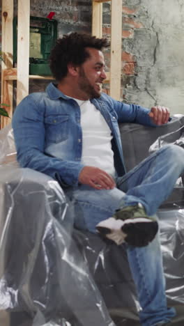 happy african-american guys discuss room restoration ideas sitting on sofa covered with plastic sheet. black friends prepare to repair house