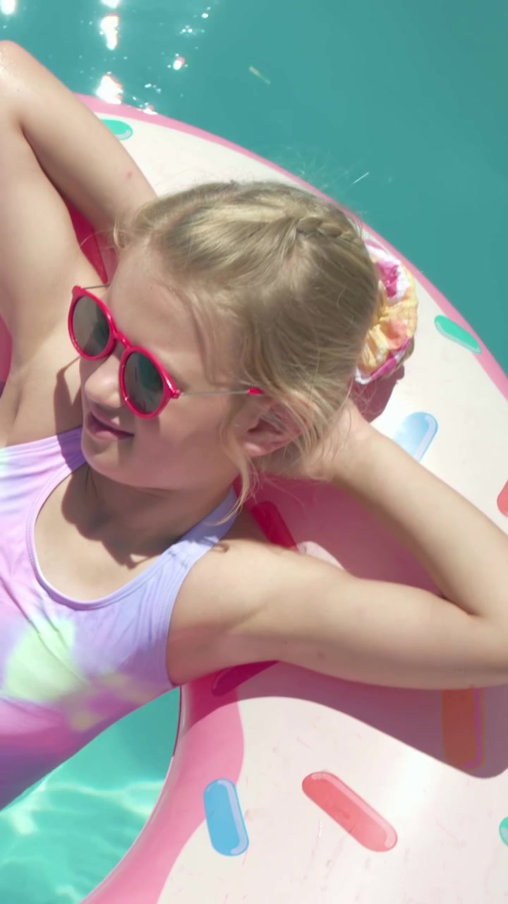 Vertical video: Lying girl turning head, relaxing as camera moving closer over pool, swimsuit donut